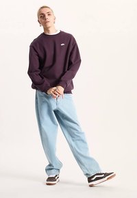 Paarse sweatshirt met logo, lichtblauwe wijde jeans, zwart-witte sneakers. Soepele textuur en ontspannen pasvorm. Casual streetwear-stijl.