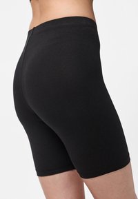 Melnas kokvilnas šorti ar pieguļošu dizainu, kuri sniedzas līdz vidukļa augstumam, ar gludu tekstūru un elastīgu jostasvietu.