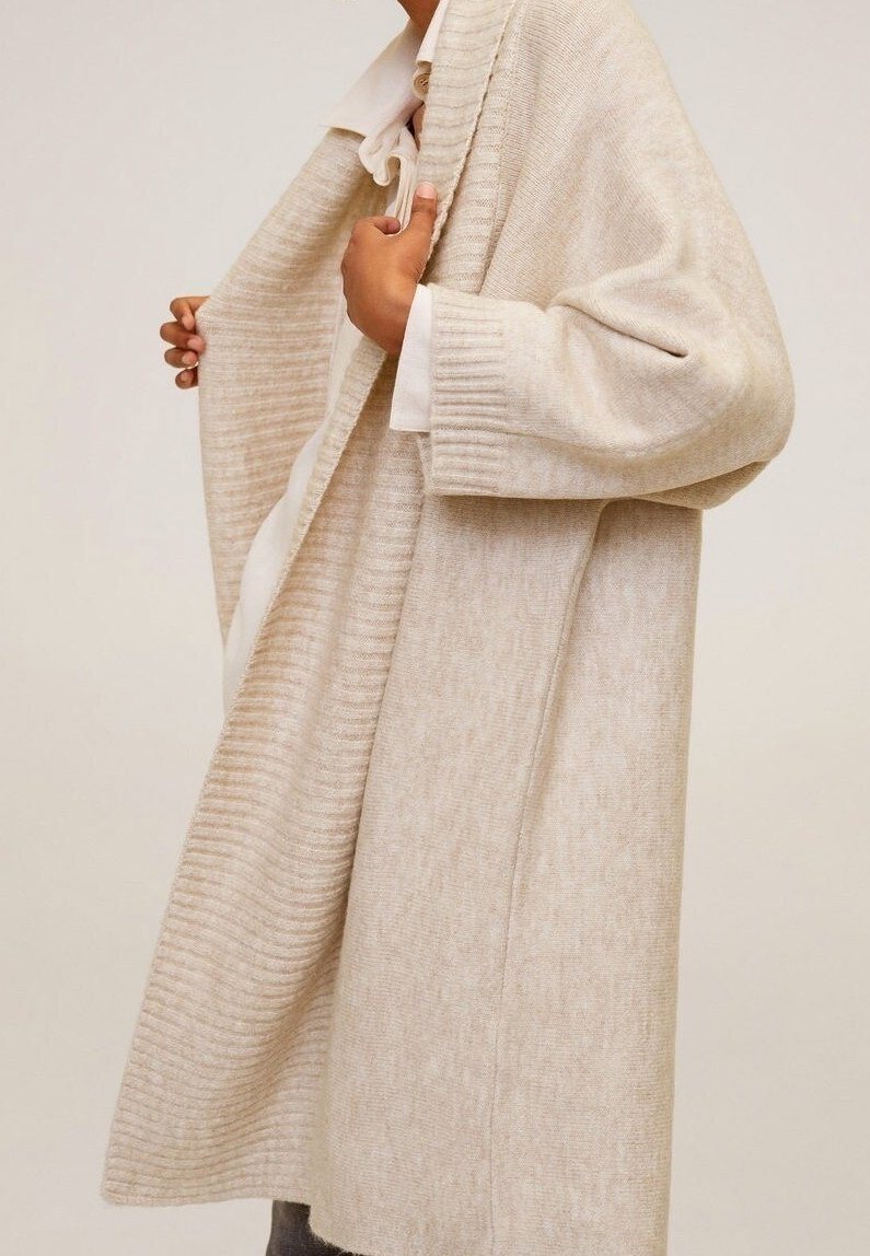 Cardigan long beige en maille douce, présentant une texture côtelée, une ouverture à l'avant et des manches larges. Design simple et élégant.