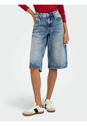 Personne portant un short en jean bleu délavé mi-long, des baskets blanches avec des rayures noires, et un haut rouge à manches longues visible aux manches.