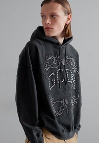 Felpa nera con cappuccio caratterizzata da un design decorativo con strass. Tessuto morbido, vestibilità comoda e elementi grafici distintivi.