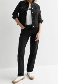 Svart denimjacka med silverknapstängning, kombinerad med svarta jeans och vita sneakers med bruna detaljer. Korta ärmar uppvikta.