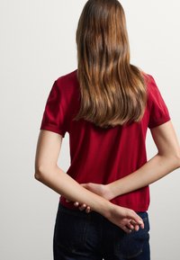 T-shirt rossa a maniche corte in una vestibilità comoda, realizzata in un tessuto morbido. Abbinata a jeans blu scuro, con cuciture visibili e un colletto semplice.