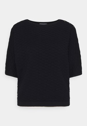 Haut noir en maille texturée à manches courtes avec col rond et trois petits boutons sur l'épaule gauche sur fond blanc.