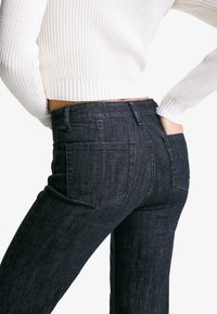 Blugi negri din denim cu talie înaltă, cu buzunare clasice la spate, având o textură subtilă și o croială slim; asortați cu un pulover alb din tricot cu model în dungi.