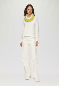 Witte lange mouw top, witte wijde broek en een gele loop sjaal. Soepele stof, losse pasvorm, minimale details en een gehaakte sjaal.