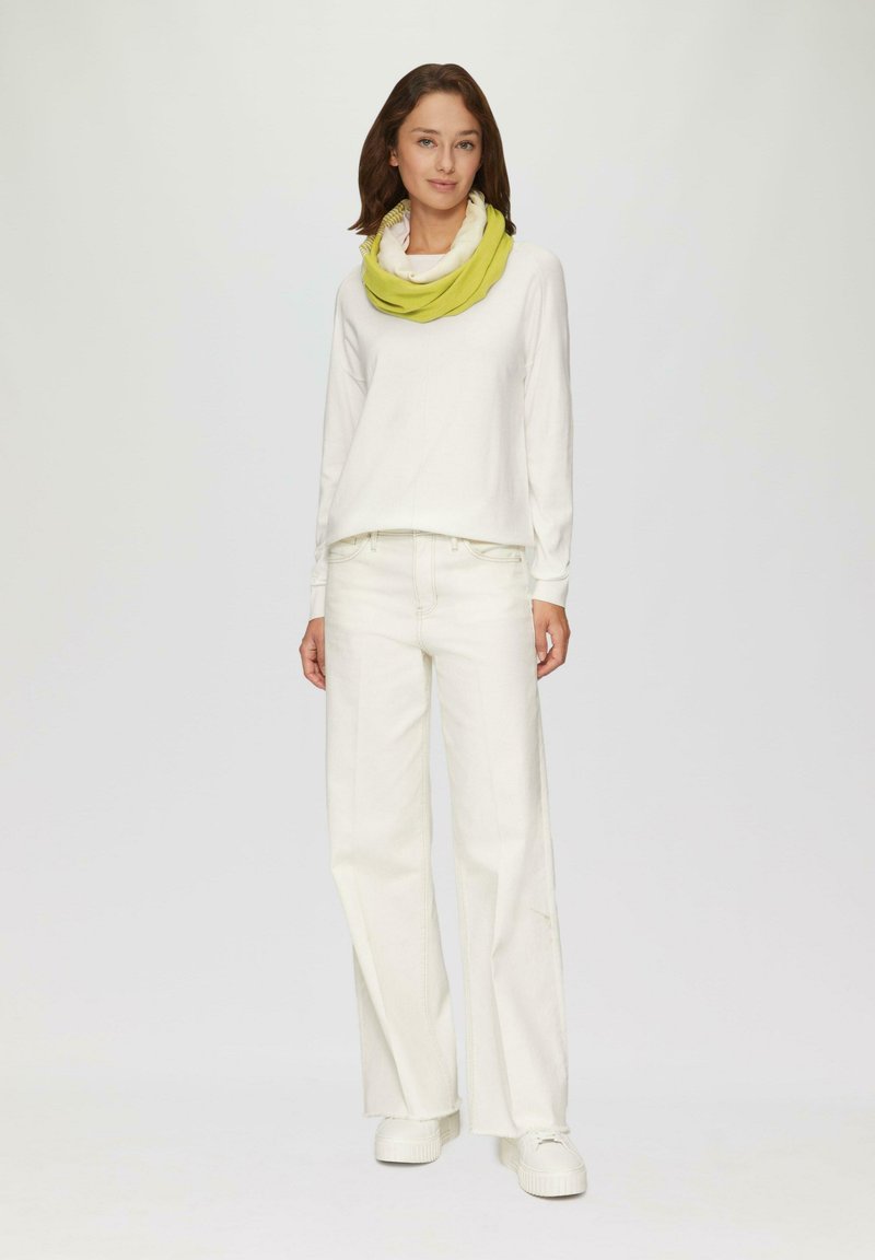 Witte lange mouw top, witte wijde broek en een gele loop sjaal. Soepele stof, losse pasvorm, minimale details en een gehaakte sjaal.