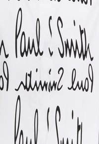 Witte stof met een herhalend zwart handgeschreven tekstpatroon dat "Paul Smith" in variërende groottes en oriëntaties weergeeft.