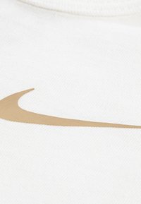 Tissu blanc à la texture lisse arborant un logo Nike swoosh doré proéminent. Le design est simple et moderne, mettant en valeur le logo.