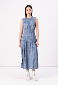Blue floral maxi dress with gathered detailing at the neckline and waist, featuring a flared skirt. Paired with white high-top sneakers and a handbag.
