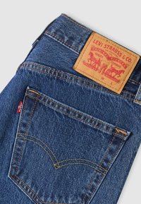 Μπλε τζιν Levi's, διπλωμένο, που δείχνει την πίσω τσέπη με πορτοκαλί ραφή και δερμάτινη ετικέτα Levi Strauss & Co. στη μέση.