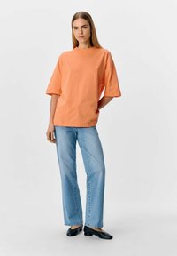 Camiseta de algodón naranja de gran tamaño con mangas cortas, combinada con jeans rectos de color azul claro y zapatos negros de tacón bajo.