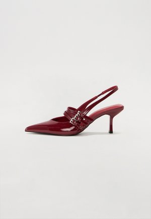 Red patent leather slingback heels with a pointed toe, two buckle straps, and a slim, mid-height stiletto heel. Smooth texture.