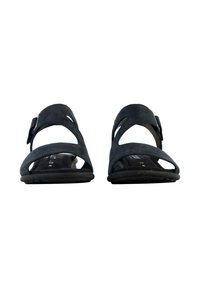 Sandale noire avec un design découpé et une sangle réglable, fabriquée en matériau doux. Elle présente une semelle plate et un fond de chaussure texturé.