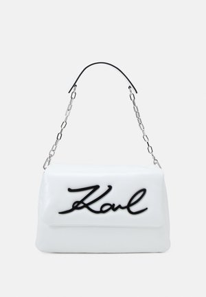 Hvid faux lædertaske med et sort "Karl" logo, der har en sølvkedestrop og glat tekstur. Rektangulær form.