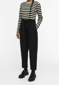 Pantalons noirs taille haute avec une ceinture à nouer, associés à un haut à rayures noir et crème à manches longues. Des chaussures noires chunky complètent la tenue.