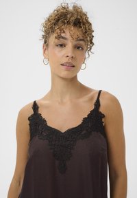 Camisole in diepbruin satijn met zwarte kantdetails bij de halslijn. Verstelbare spaghettibanden en een vloeiende silhouette.