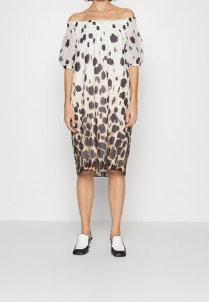 Off-shoulder knælængde kjole med sorte og brune uregelmæssige pletter og puffede ærmer, kombineret med sorte og hvide slip-on sko.