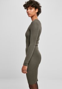 Robe tricotée côtelée vert olive, manches longues, silhouette cintrée, col rond, longueur genou, avec des fentes latérales discrètes et des détails de couture.