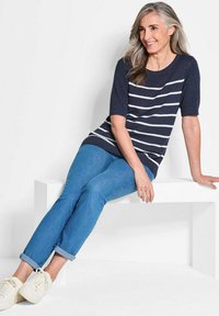 Dunkelblauer Strickpullover mit weißen horizontalen Streifen, kurze Ärmel; kombiniert mit hellblauen hochgekrempelten Jeans und weißen Sneakers.