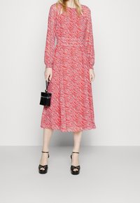 Robe midi rouge et blanche à imprimé zèbre avec des manches longues, une taille élastique et une silhouette fluide, assortie à des talons compensés noirs.