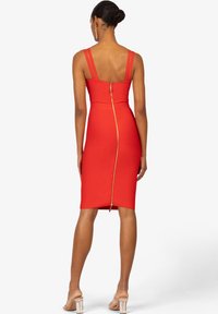 Rotes, tailliertes Kleid mit dünnen Trägern, ausgestattet mit einem Reißverschluss im Rücken, knielang und mit glatter Textur. Sichtbare Nahtdetails und klare Linien.