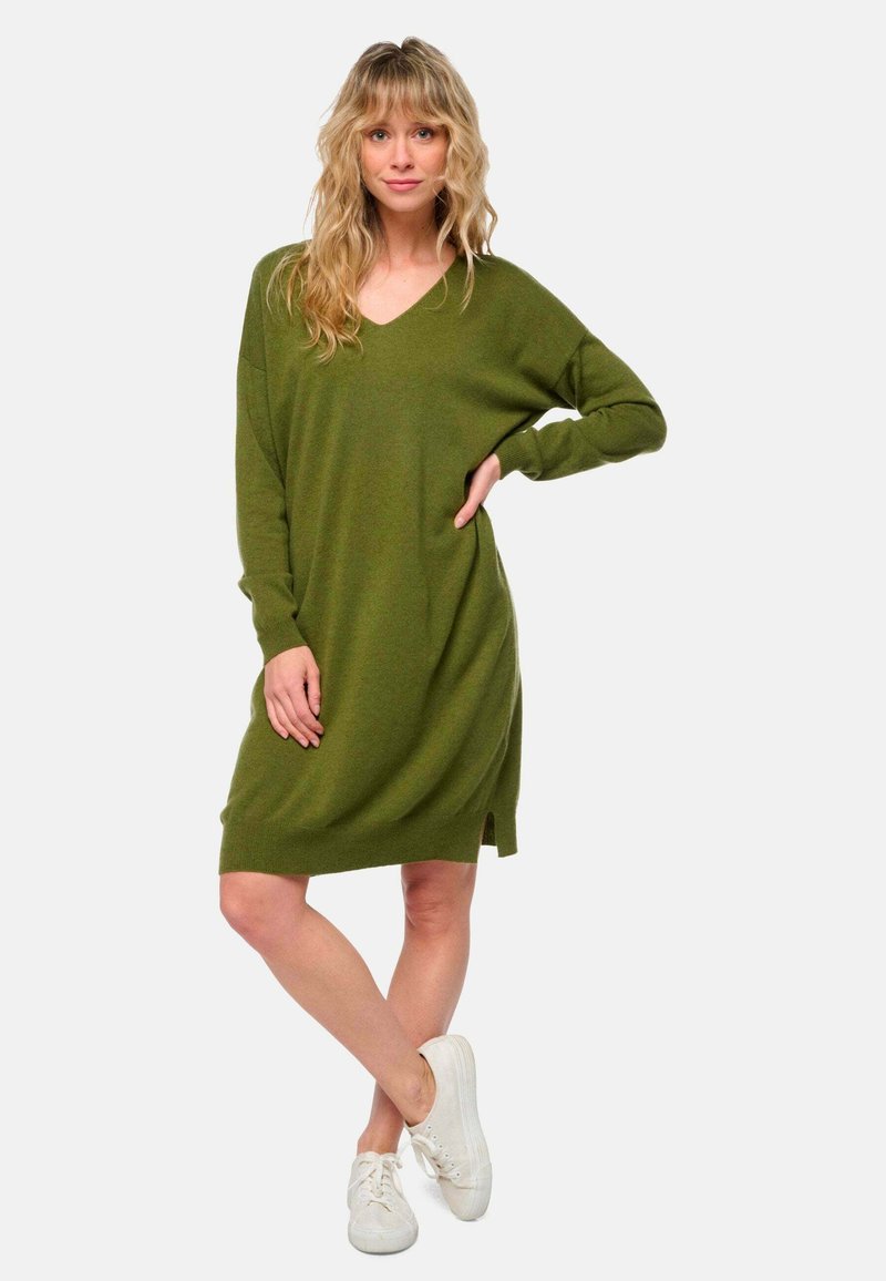 Robe tricotée vert olive avec un décolleté en V et des manches longues, dotée de fentes sur les côtés en bas. Associée à des baskets blanches.