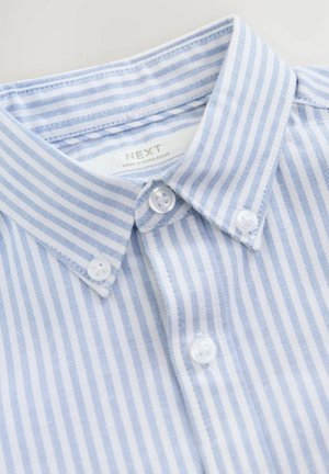 Chemise à rayures bleues claires et blanches avec un col boutonné, présentant deux boutons blancs sur la patte de boutonnage et une étiquette cousue à l'intérieur.