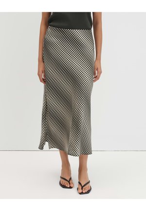 Donna che indossa una gonna midi con motivo geometrico bianco e nero e sandali neri con cinturini, in piedi davanti a uno sfondo semplice.