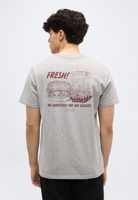 Άνδρας που φορεί γκρι μπλουζάκι με γραφικό σχέδιο vintage στυλ από μπέργκερ, τηγανιτές πατάτες και ποτό και κείμενο «ΦΡΕΣΚΟ! Δεν υπάρχει υποκατάστατο για τα κλασικά.»