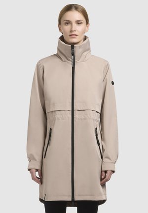 Beige Knielanger Mantel mit hohem Kragen, Reißverschluss vorne und zwei Seitentaschen. Mit schwarzen Reißverschluss- und Knopfakzenten. Glatte Stoffstruktur.