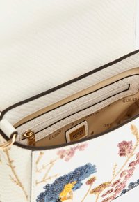 Bolso blanco de piel sintética con bordado floral en azul, rosa y amarillo; interior espacioso beige con un bolsillo con cremallera y marca.