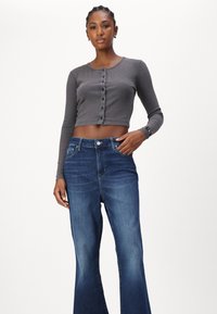 Γκρι ριγωτό, μακρυμάνικο crop top με κουμπιά, σε συνδυασμό με ψηλόμεσα, φαρδιά μπλε τζιν. Και οι δύο υφές υφάσματος είναι ορατές.