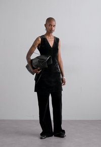 Rochie neagră fără mâneci, cu un decolteu adânc în V, purtată împreună cu o pereche de pantaloni negri cu picioare late. Ține o geantă mare neagră. Material neted și siluetă modernă.