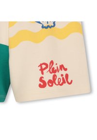 Κοντομάνικο πουκάμισο σε εκρού με πράσινες λεπτομέρειες. Διαθέτει κίτρινο κυματιστό σχέδιο, μπλε γραφικό με κοχύλι και κόκκινο κείμενο «Plein Soleil». Κατασκευασμένο από βαμβά κι.