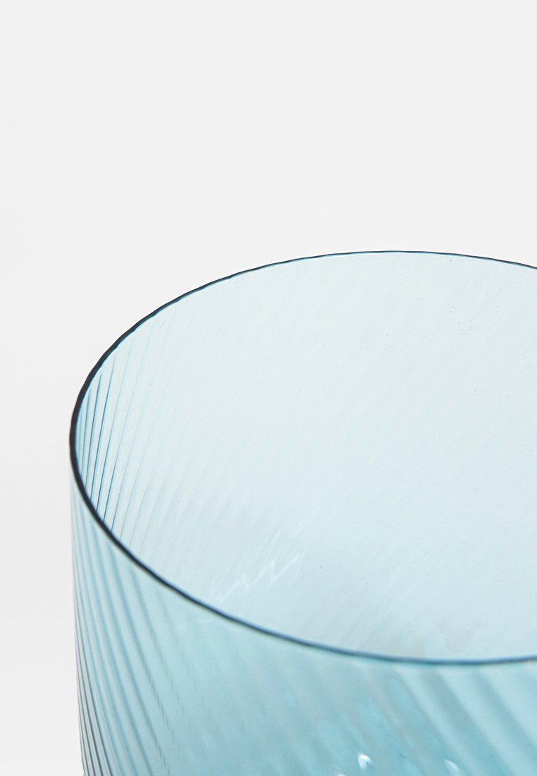 Vidrio azul claro translúcido con textura acanalada vertical; abertura circular con borde suave que resalta el diseño y la artesanía.