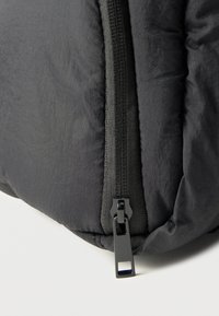 Κοντινό πλάνο μαύρου φερμουάρ σε επενδεδυμένη, σκοτεινή υφασμάτινη επιφάνεια, μερικώς κλεισμένο, με ορθογώνια ταινία έλξης να ακουμπά σε λευκό φόντο.