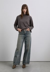 Oversized grå tröja i mjukt tyg, kombinerad med vida blekta blå jeans. Neutralt tonade spetsiga klackskor fulländar looken.