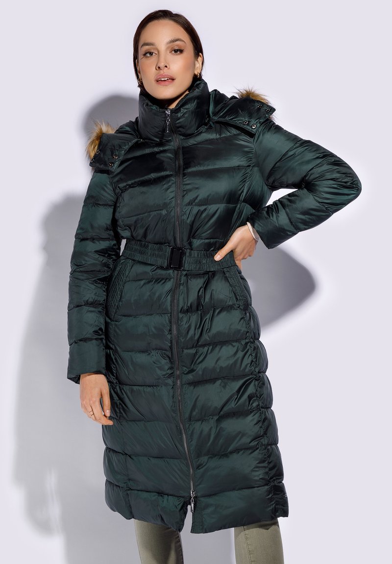 Long, dark green puffer coat with a belted waist, high collar, and fur-accented hood; features a zipper closure and horizontal quilting.
