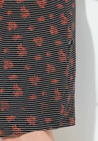 Tessuto a righe bianche e nere con motivi floreali rossi. Presenta una cucitura laterale e una piccola etichetta di tessuto vicino all'orlo. Texture morbida.