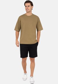 Khaki oversized t-shirt met korte mouwen, gecombineerd met zwarte shorts. Witte sneakers. Eenvoudig ontwerp, zachte stof, normale pasvorm.