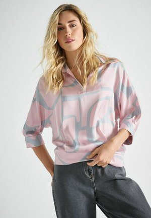 Lässige, langärmelige Bluse aus pinkem Satin mit grauen abstrakten Mustern. Verfügt über einen halben Reißverschluss am Kragen und eine weiche Textur, kombiniert mit dunklen Jeans.