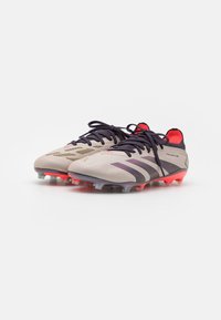 Lichtgrijze voetbalschoenen met donkerpaarse accenten en rode details. Dit paar heeft een gestructureerde bovenkant en doorzichtige gripnoppen op de zool.