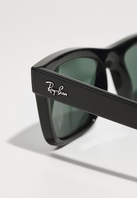Ray-Ban solglasögon med svarta plastbågar, gröna linser och silverdetalj med logotyp på skalmen. Rektangulär design med slät yta.