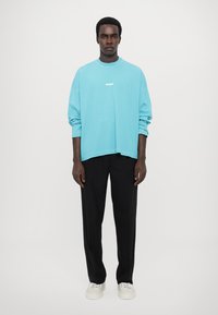 Light blue oversized sweatshirt with white logo, paired with black tailored pants and white sneakers. Smooth fabric with relaxed fit.
