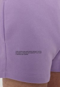 Lilla økologisk bomullsshorts med jevn tekstur. Har svart tekstdetalj om stoffbehandling nederst på venstre side.