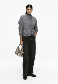 Grauer Cardigan mit hohem Kragen, strukturierter Strickware und Knopfverschluss. Kombiniert mit schwarzen Weitbeinhosen und einer kleinen beige Handtasche mit Schlangenprint.