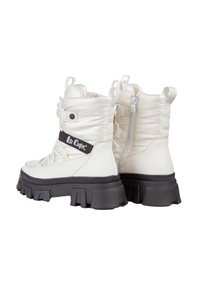 Białe ocieplane botki za kostkę z masywną czarną podeszwą, zamek błyskawiczny i detale w postaci pasków. Materiał wydaje się być syntetyczny o gładkiej fakturze.