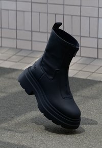 Zwarte enkellaarsjes van glad leer met een chunky plateauzool, voorzien van een zijrits en lusje voor gemakkelijk aan- en uitrekken.