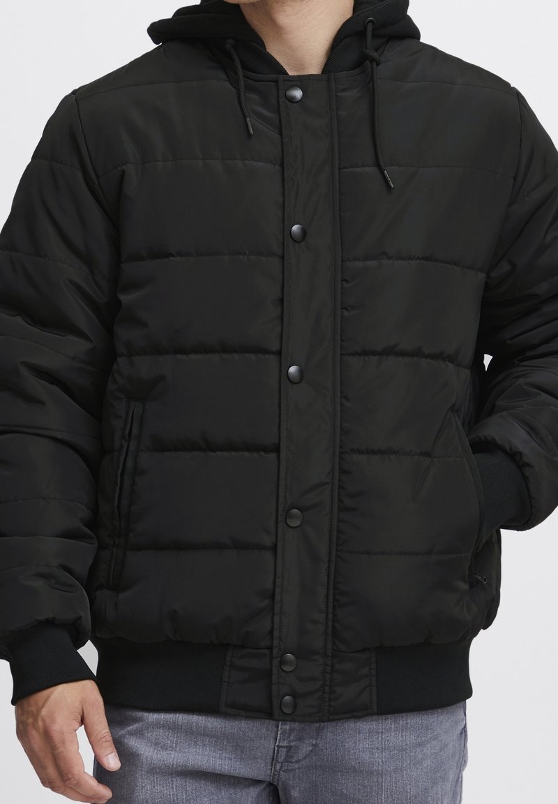 Czarna kurtka puchowa z podszytym kapturem, zapięciem na zatrzaski, ściągaczami na mankietach i dole, pikowaną fakturą oraz bocznymi kieszeniami.